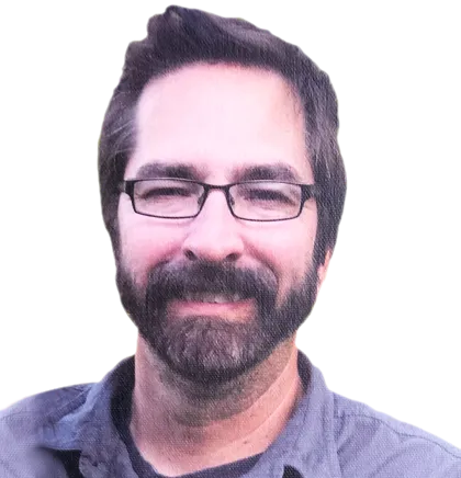 A man with dark hair and a beard is wearing glasses and a grey shirt, smiling warmly at the camera, possibly after enjoying one of the exciting Chicago Brewery Tours.